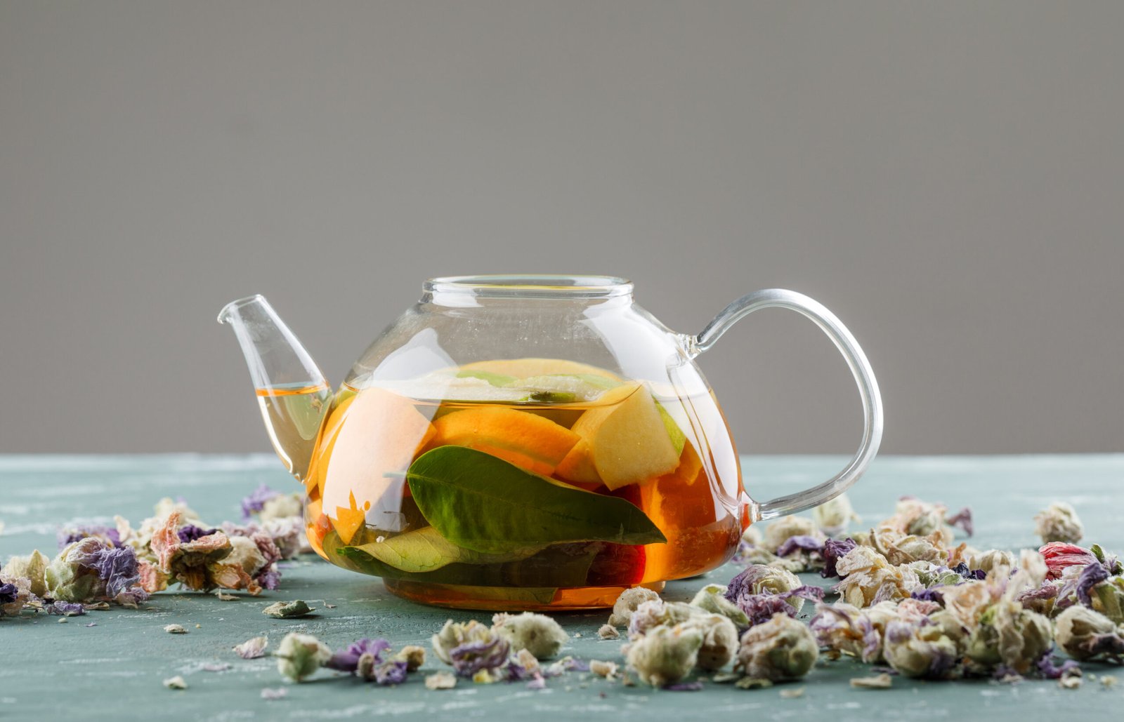 Fruit infused water in a teapot with dried flowers side view on plaster and grey background